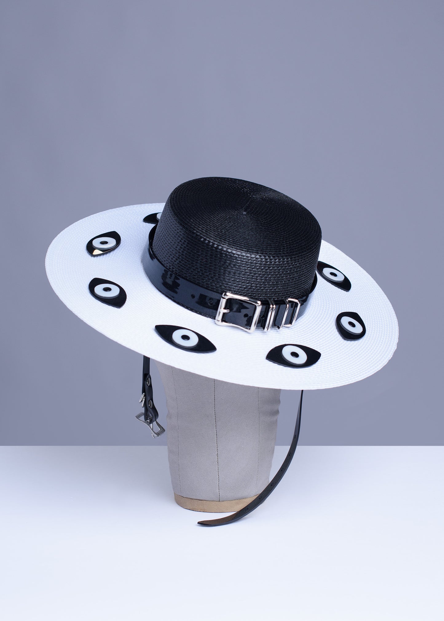 Apatico harness hat with wide brim. Black and white two-tone faux strap. Eyeball design all around the brim.